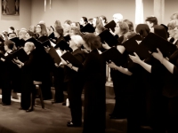 Black and white photo of the chorus, in all black, holding folders singing