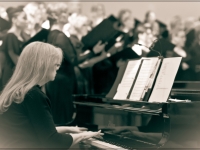 black and white photo of the accompanist at the piano with the chorus singing in the background