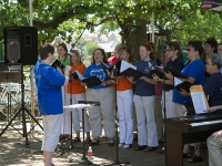 The chorus sings at Central Market under the shade of a big tree